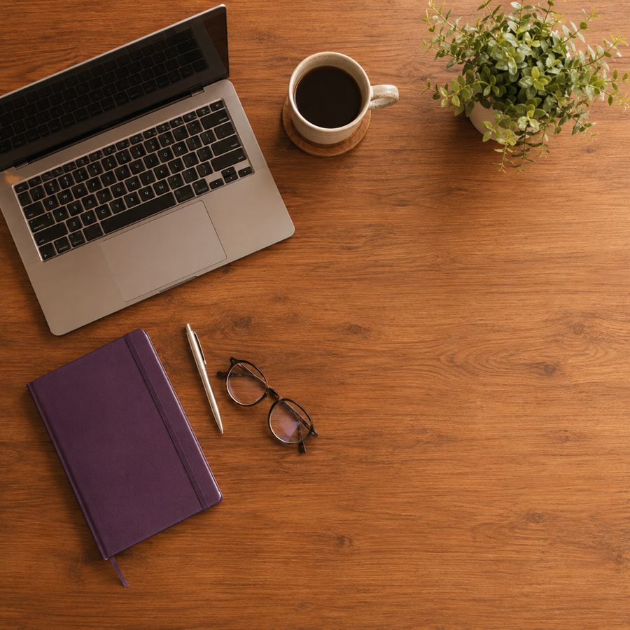 Mesa de trabalho simples vista de cima, com notebook, caderno e uma xícara